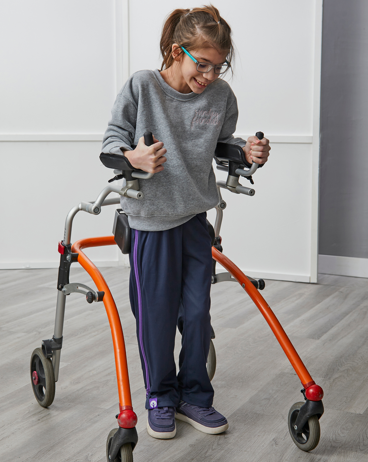 Person using a walker with orange legs in a room.