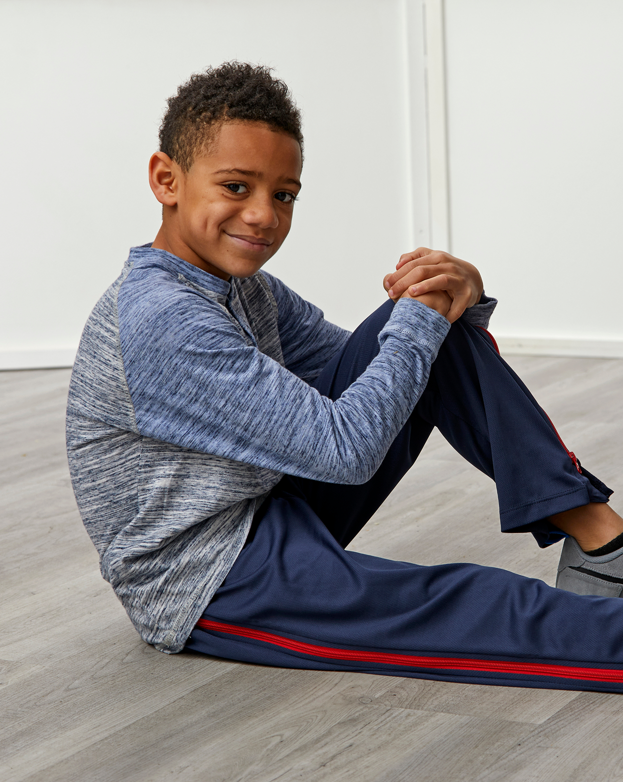Child sitting on the floor wearing a blue and gray athletic outfit with red accents.