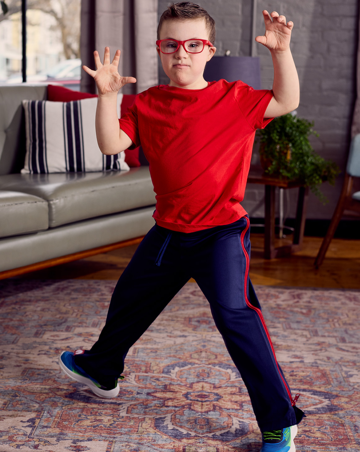 Child in red shirt and blue pants with red stripes in a living room