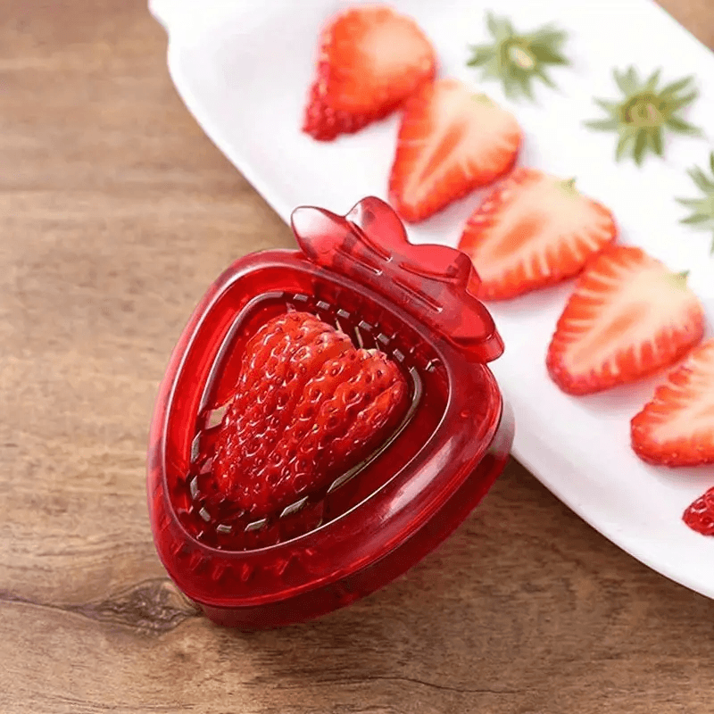 Red strawberry-shaped mold on a wooden surface with sliced strawberries in the background.