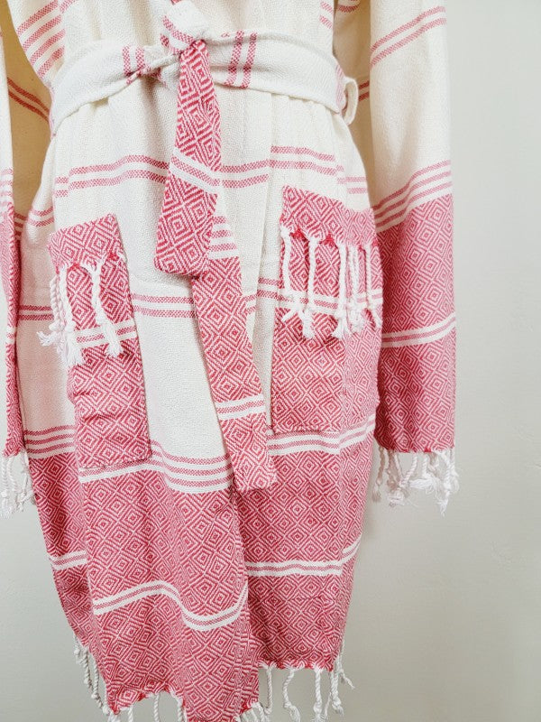 Unisex hooded bathrobe close-up: cream fabric with pink geometric panels and tassel trim hem.