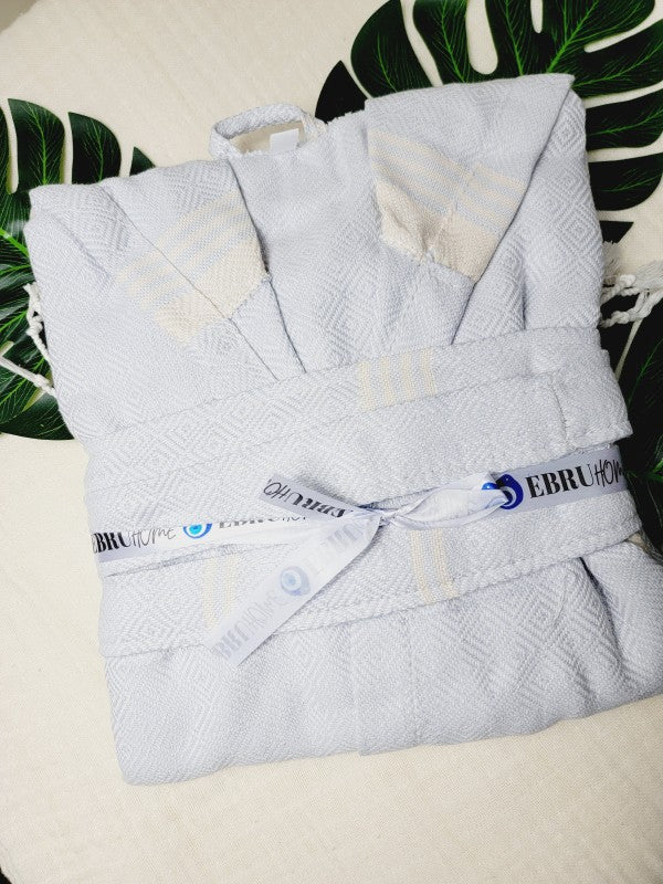 Folded off-white hooded robe with belt, patch pockets, and tassel-trim detail