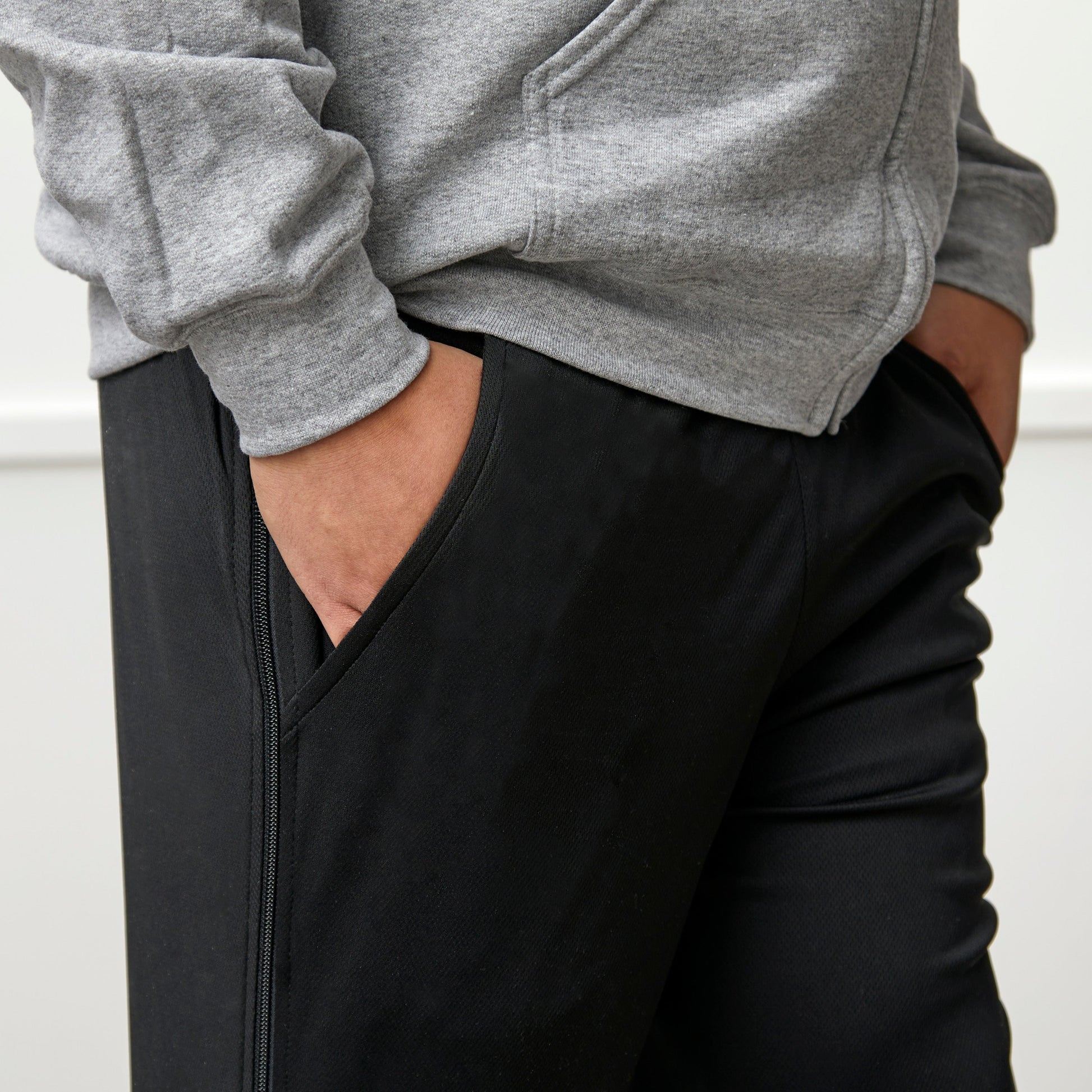 Person wearing a gray hoodie and black pants with a white background