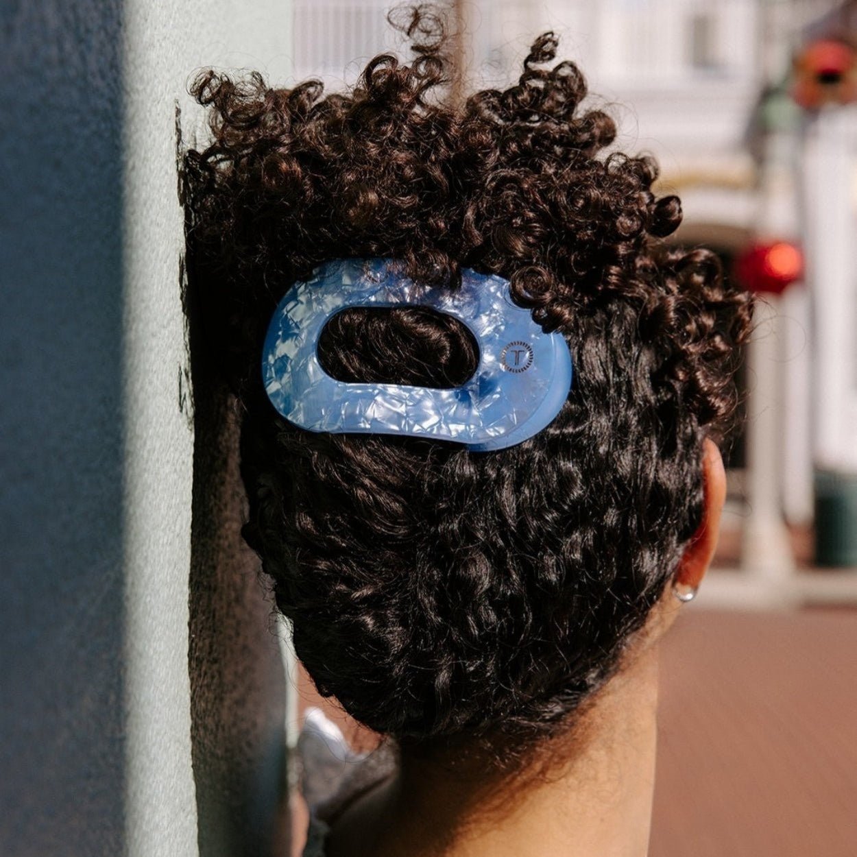 Large light blue hair clip with oval center holding curly dark hair