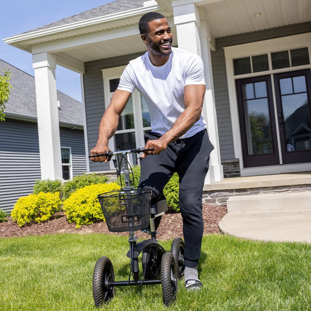 Person riding an all-terrain knee walker with basket and padded knee support outdoors