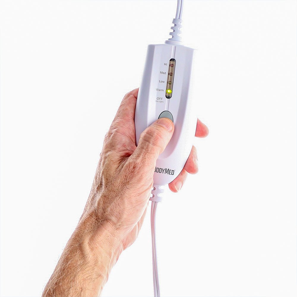 Hand holding white controller with LED indicator over blue heating pad