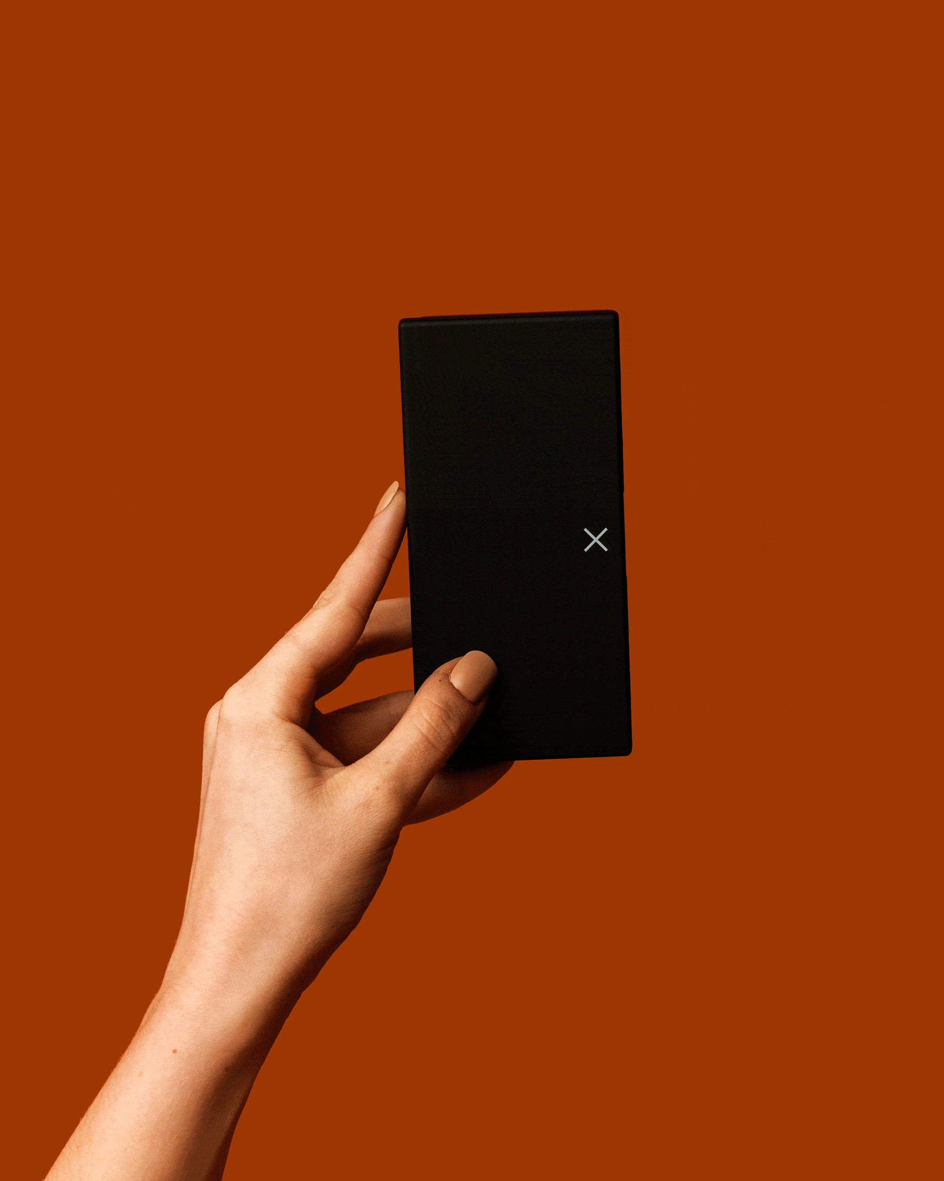 Black rectangular pill box held in hand, X logo on closed front