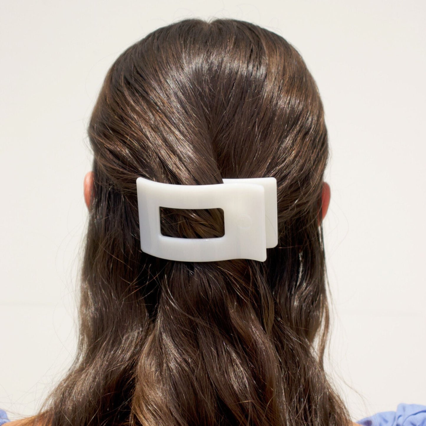 Small flat rectangle hair clip in white, clipped onto dark brown hair