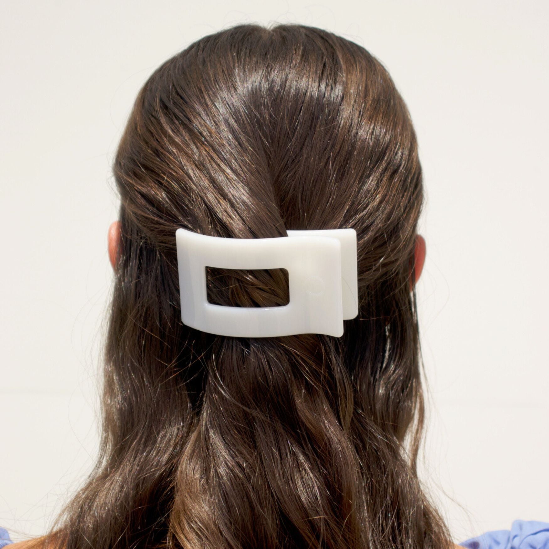Small flat rectangle hair clip in white, clipped onto dark brown hair