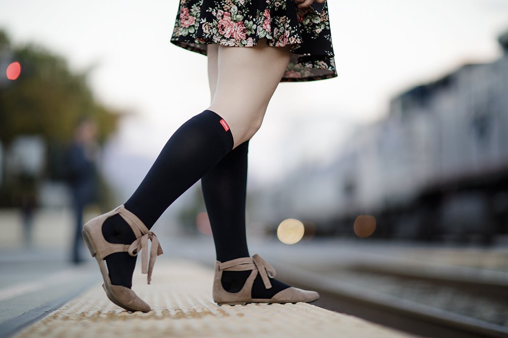 Black compression socks worn with beige heels, logo at top cuff