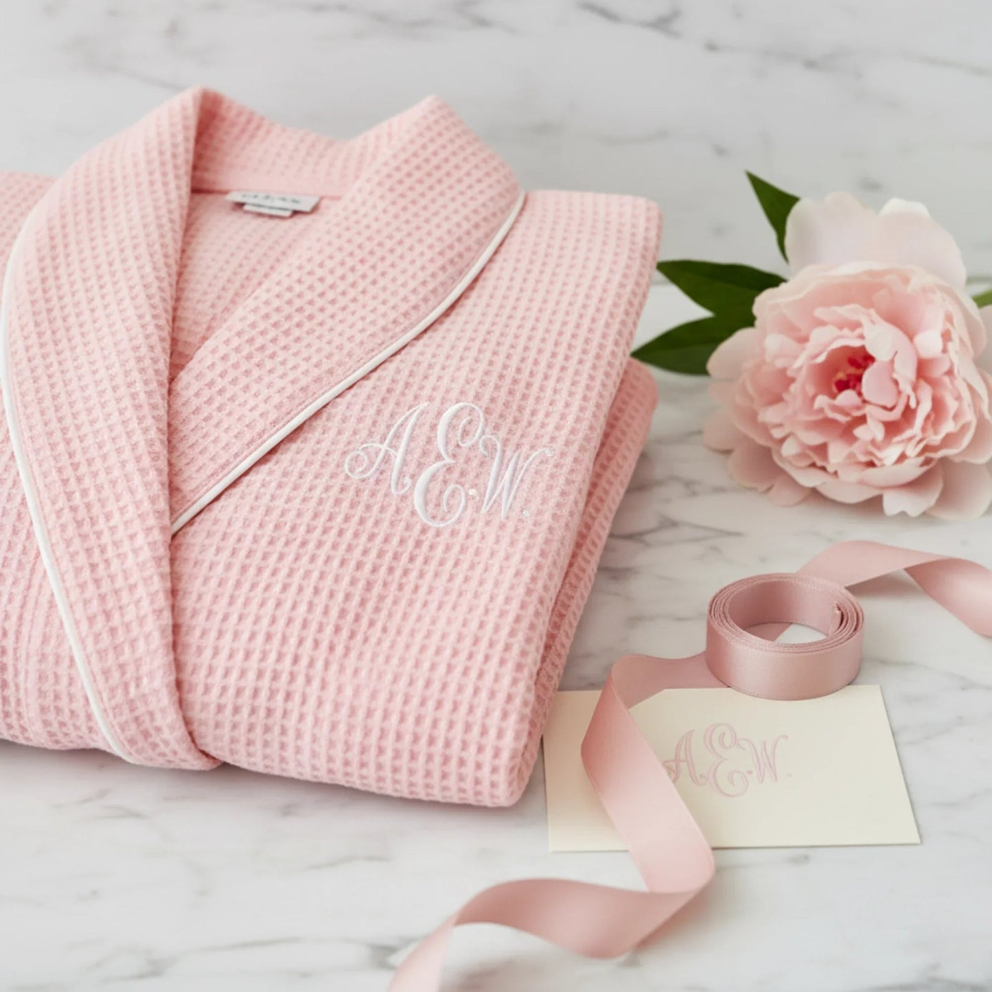 Women’s waffle bathrobe with white piping, light blush-pink folded robe with belt.