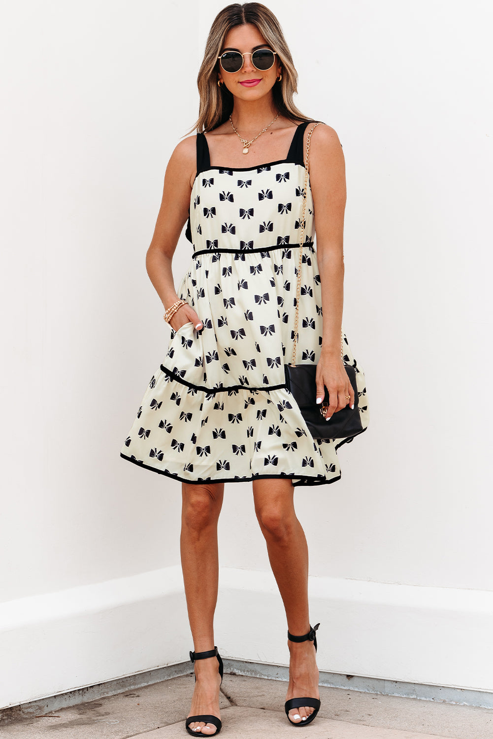 White bow-pattern mini dress with black trim, bow-knot shoulder straps, tiered skirt