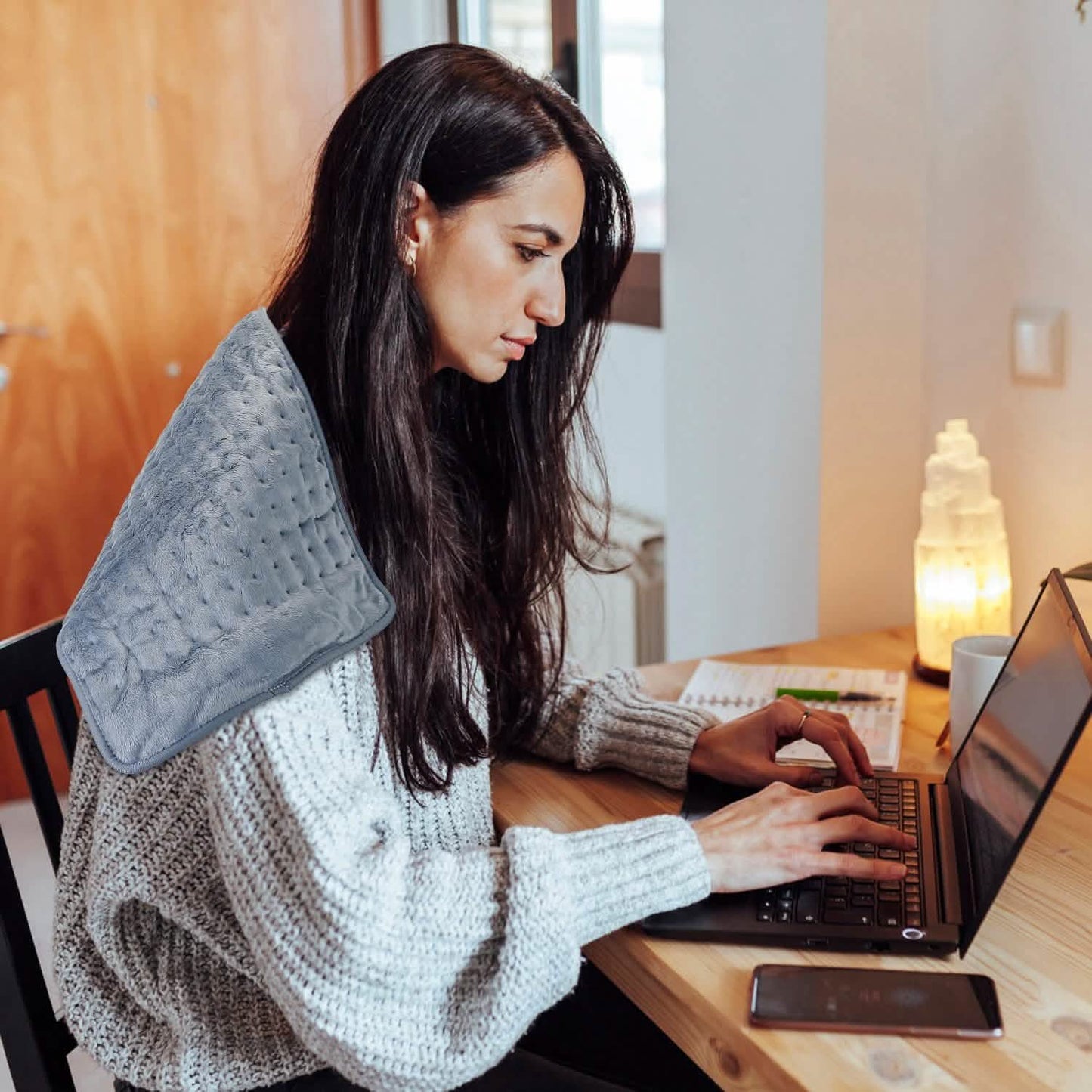 Grey electric heating pad worn on lap while seated at desk