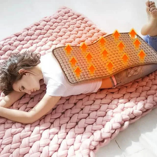 Pink heated blanket-style pad with raised dots, held over a person’s back for warmth