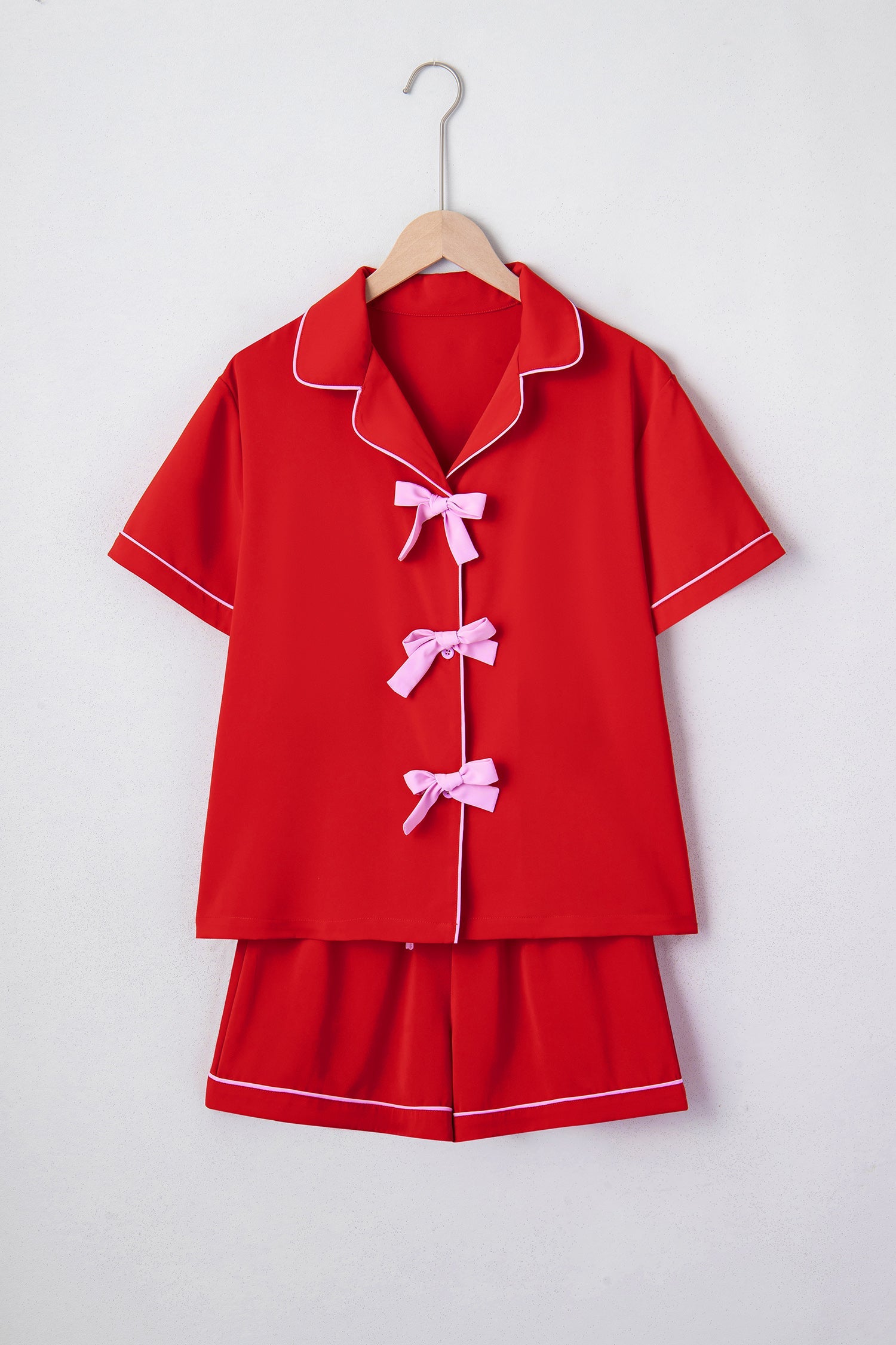 Red silky pajama set on hanger with button front, bow details, and matching shorts