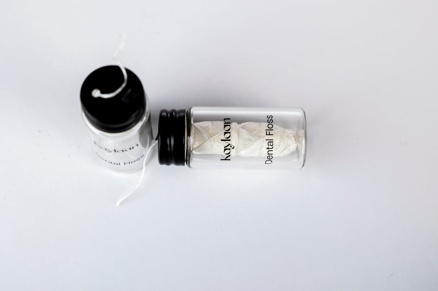 Dental floss bottle with black cap and loose white floss strands on a surface