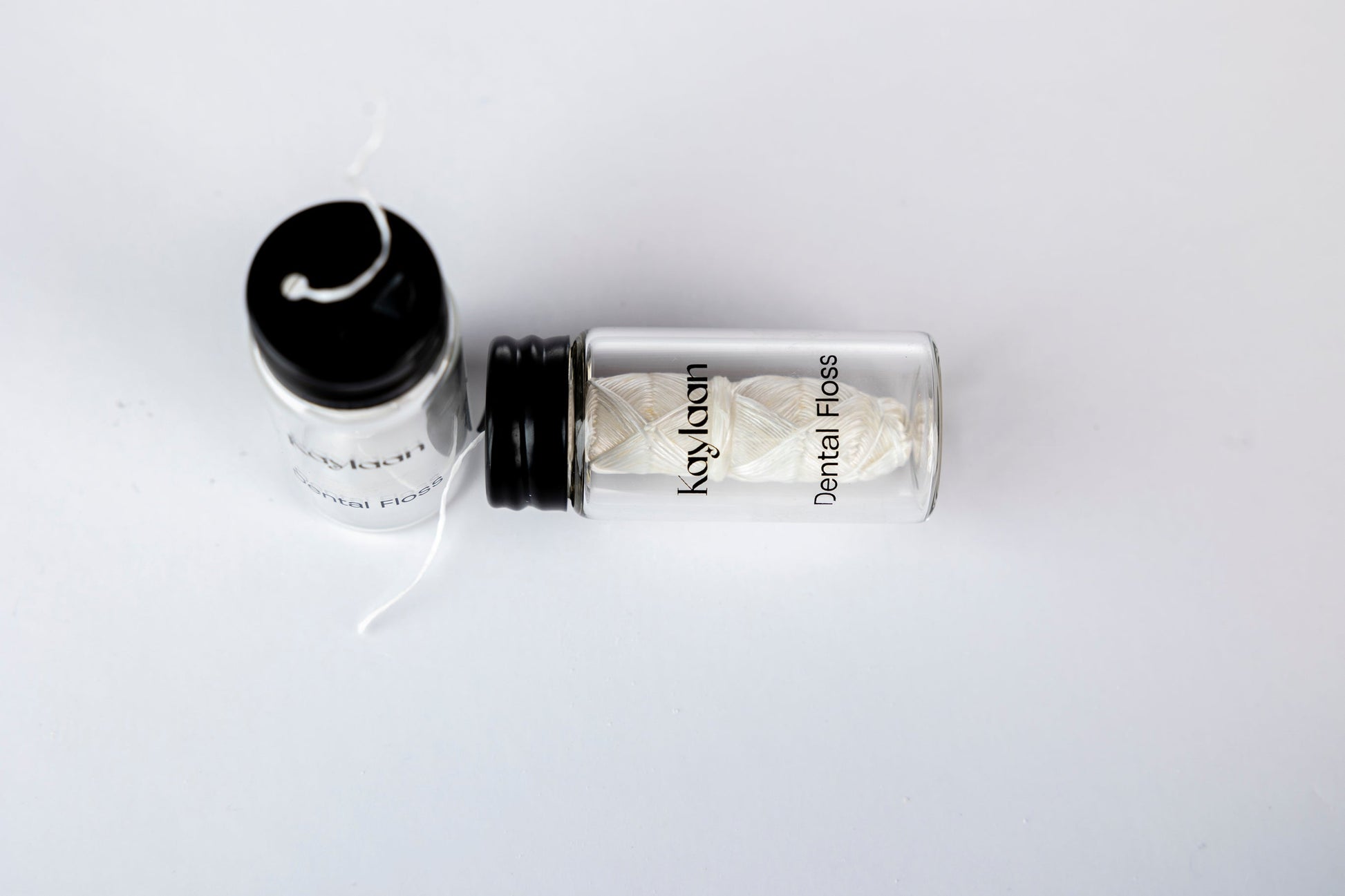 Dental floss bottle with black cap and loose white floss strands on a surface