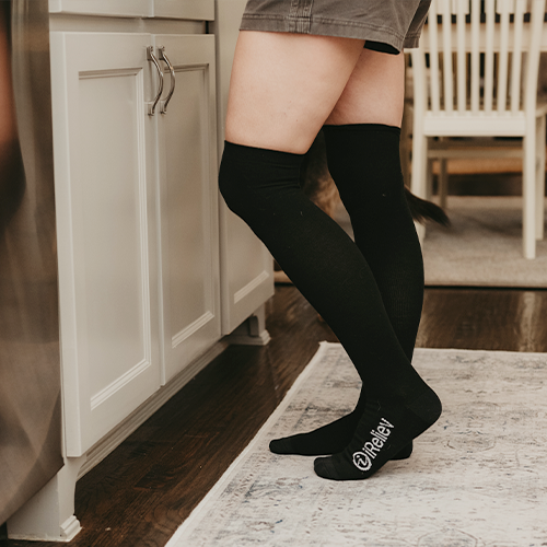 Knee-high bamboo compression socks in black, worn near a cabinet
