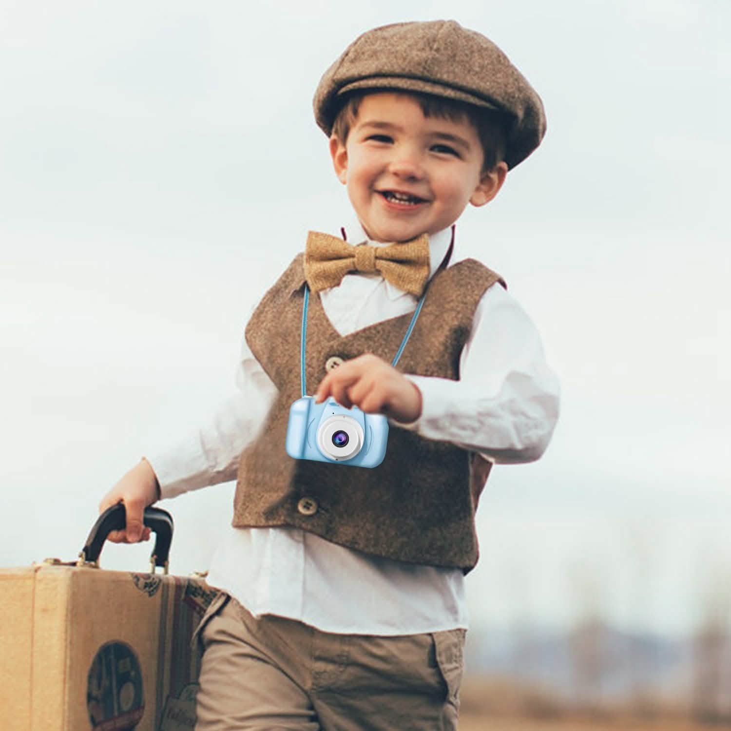 Light blue kids digital camera in a child’s hand while standing with a bag