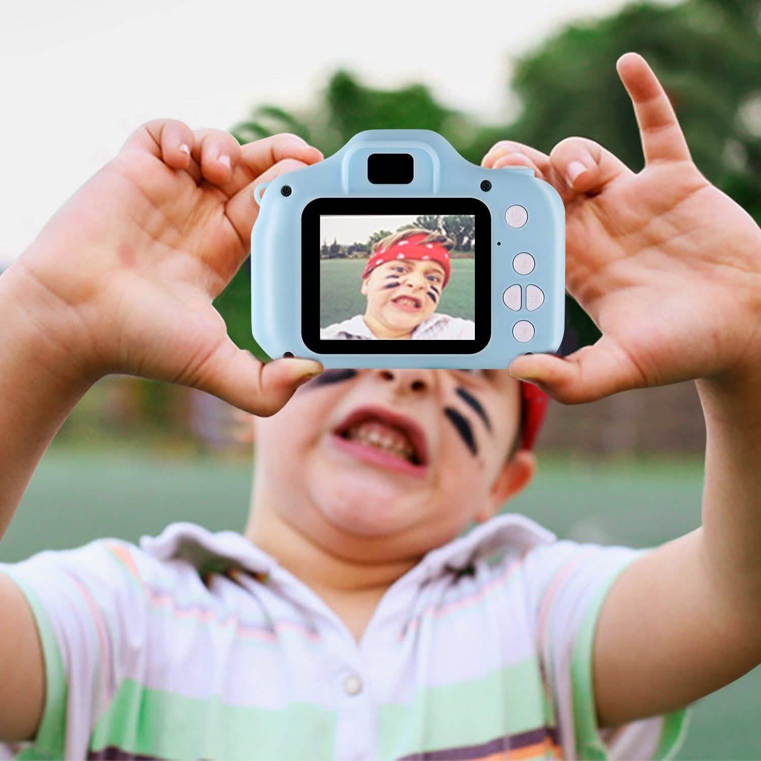 Light blue kids digital camera held up to take a photo, with child smiling behind it