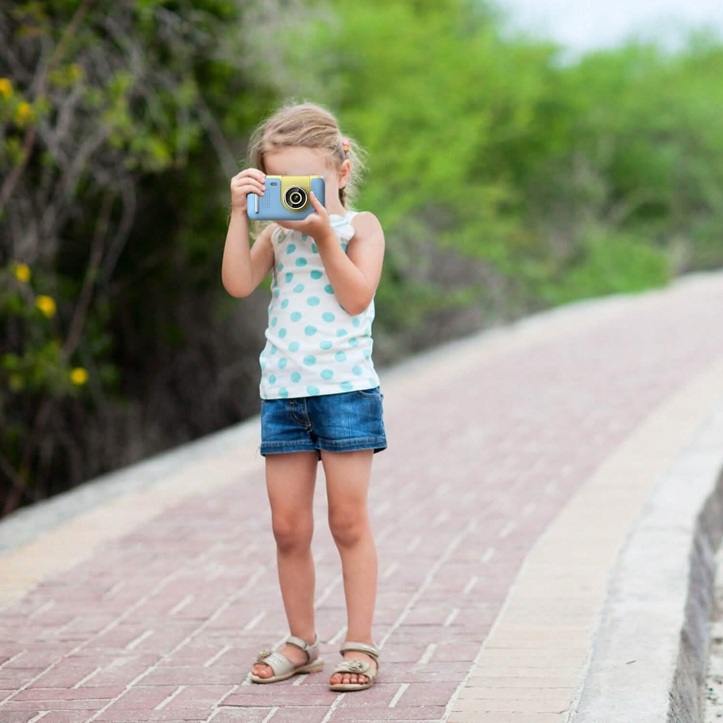 Child holding a blue kids digital camera with yellow lens, taking a photo