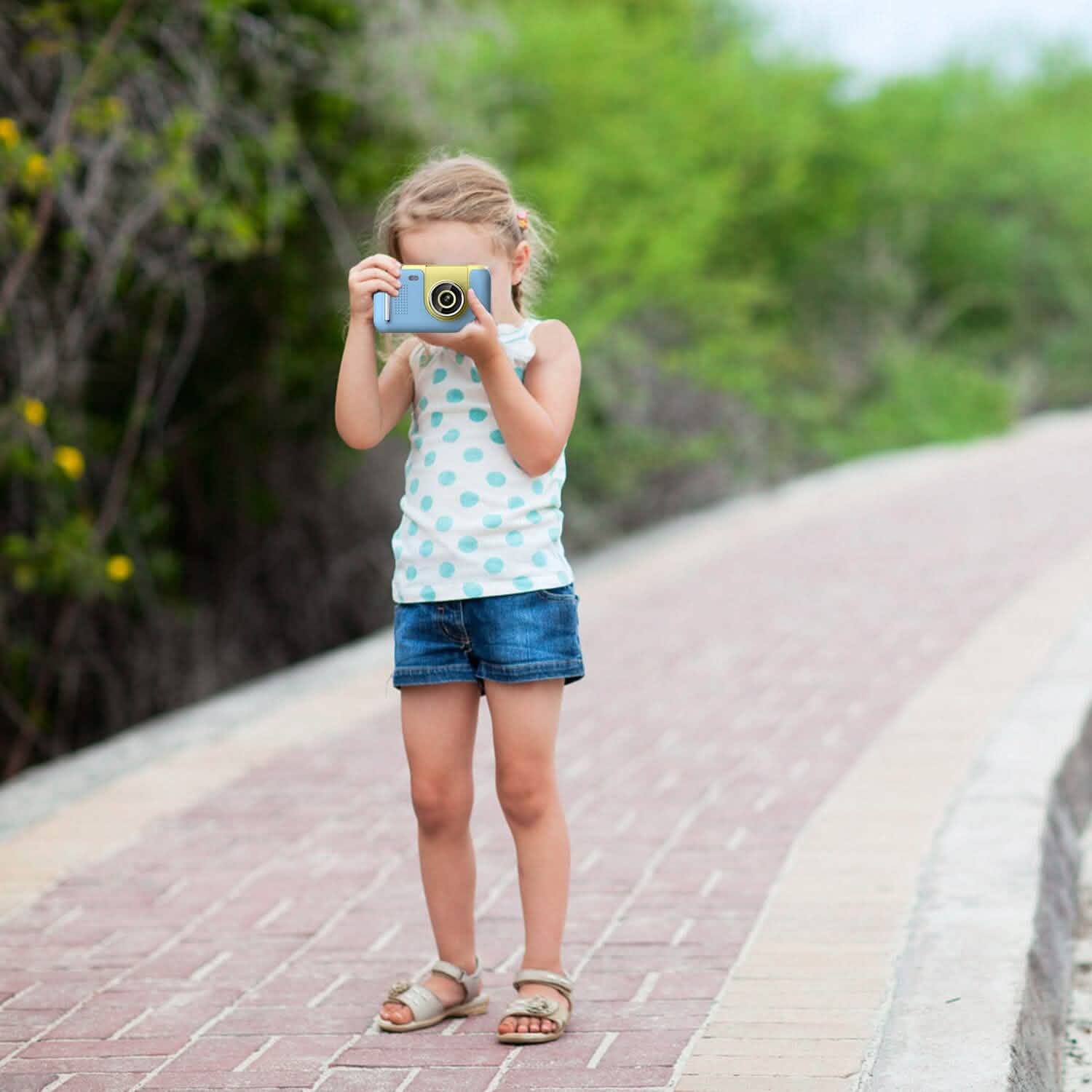 Child holding a blue kids digital camera with yellow lens, taking a photo