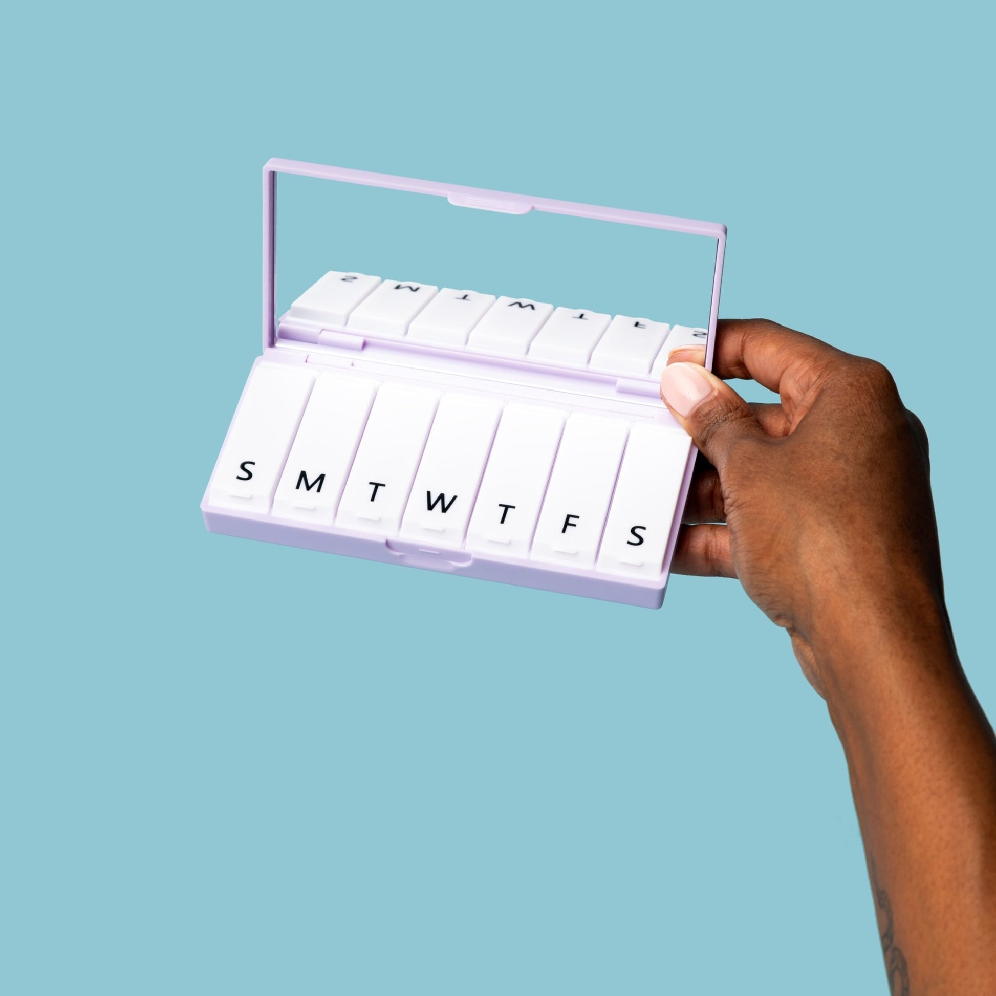 Lilac pill box open with lettered trays, held in hand