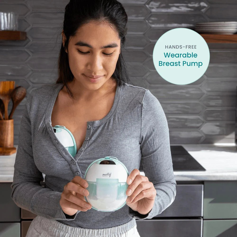 Woman wearing a wearable breast pump on her chest, holding the white mint pump dome