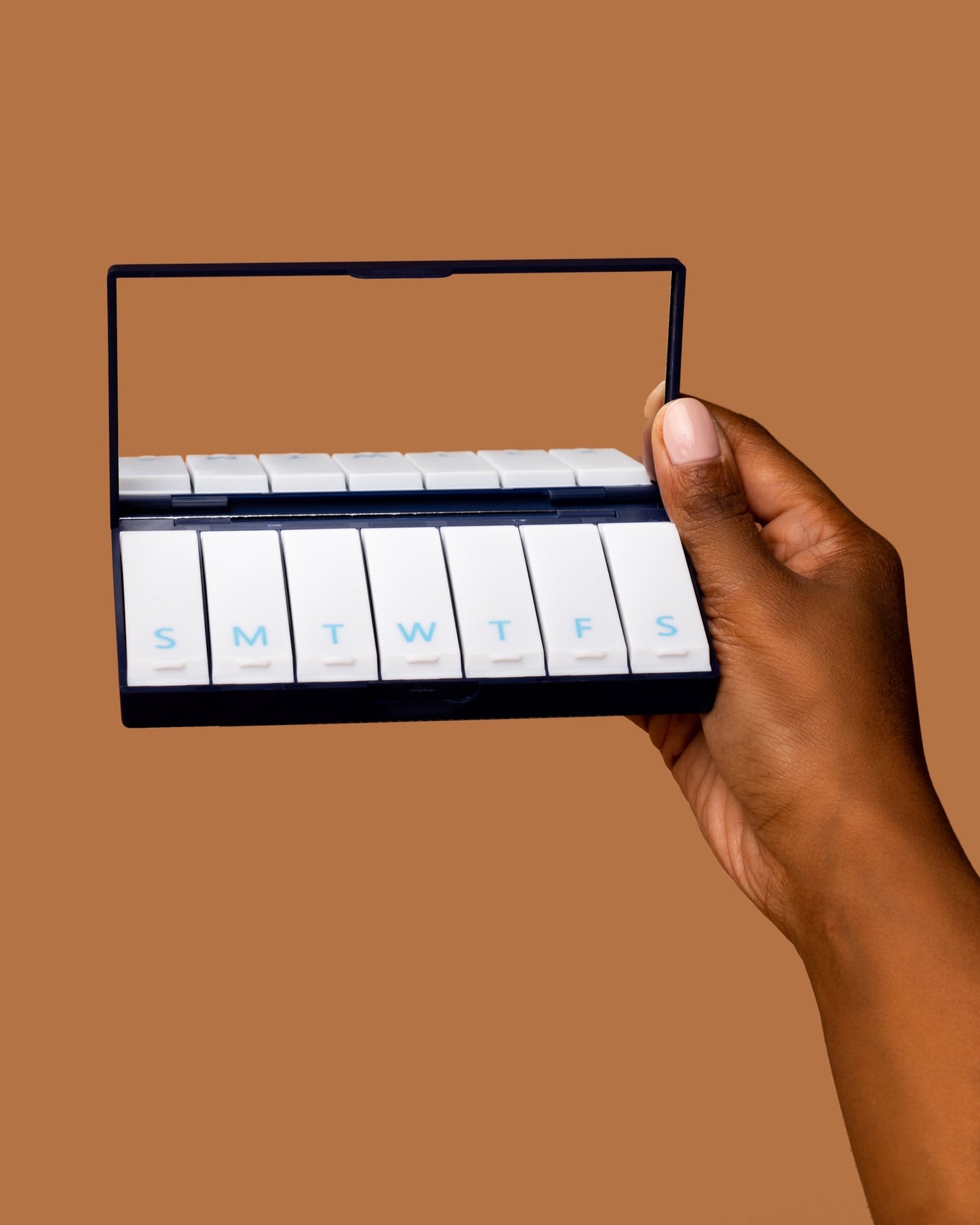 Navy blue pill box held by hand, open with labeled slots