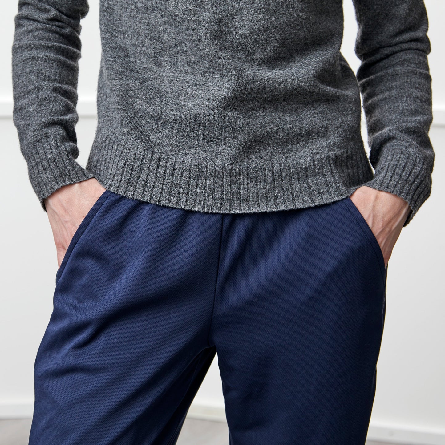 Person wearing a gray sweater and navy pants against a white background