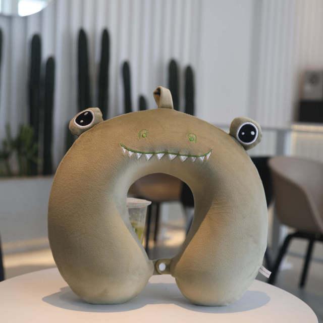 Tan U-shaped monster neck pillow with green spots and jagged tooth smile