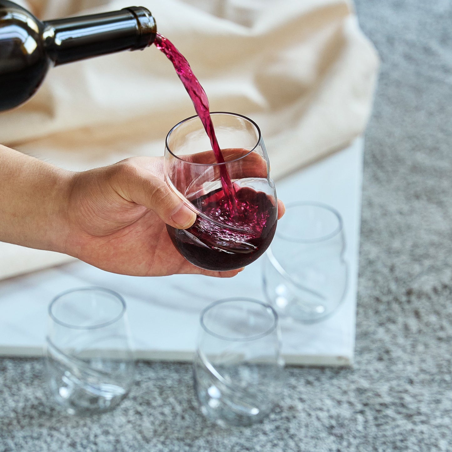 Stemless acrylic wine glass with finger indent, red wine being poured into clear cup