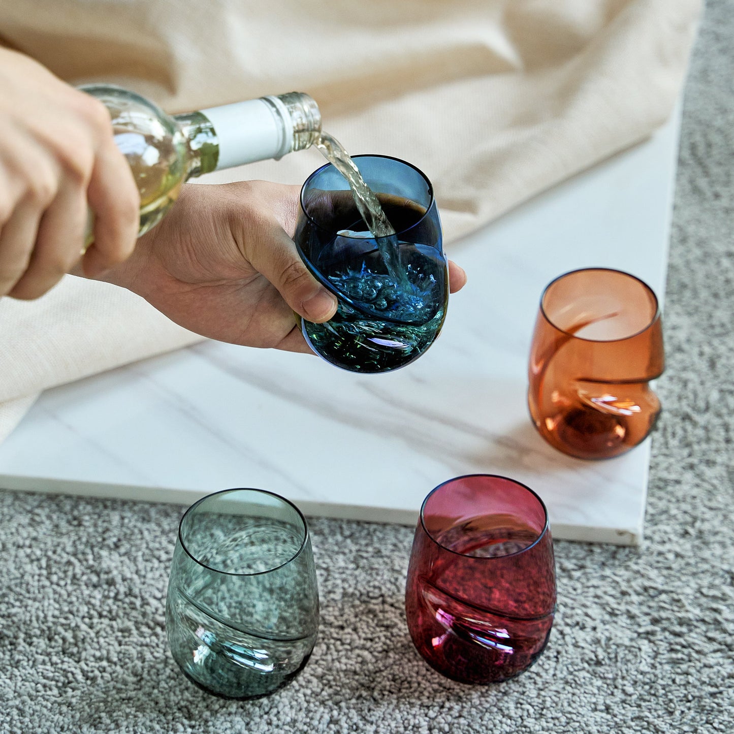Blue acrylic stemless wine glass with finger indent as wine is poured; other colored glasses