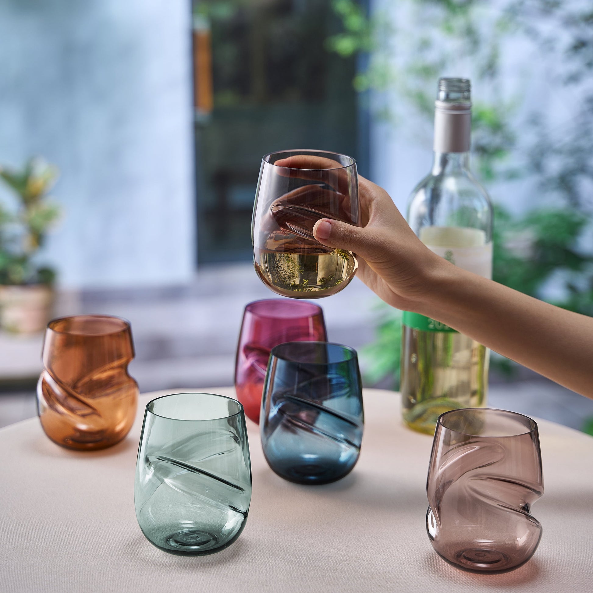 Set of 6 acrylic stemless wine glasses, finger-indented bowls; hand holds a blue glass