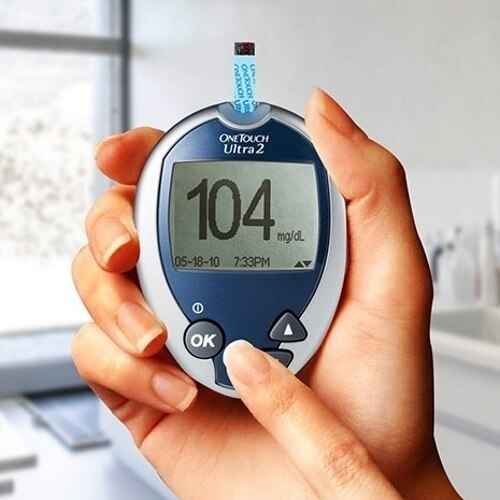 Hands holding OneTouch Ultra 2 glucose meter screen reading 104 mg/dL