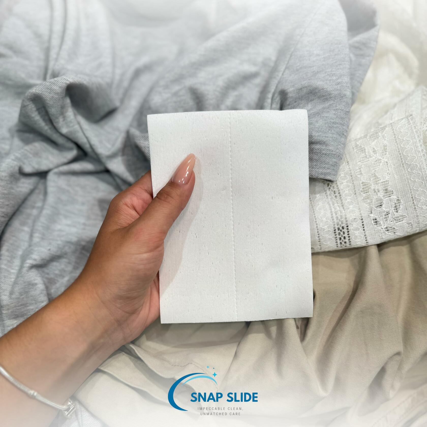 Hand holding a white laundry detergent sheet over light fabric