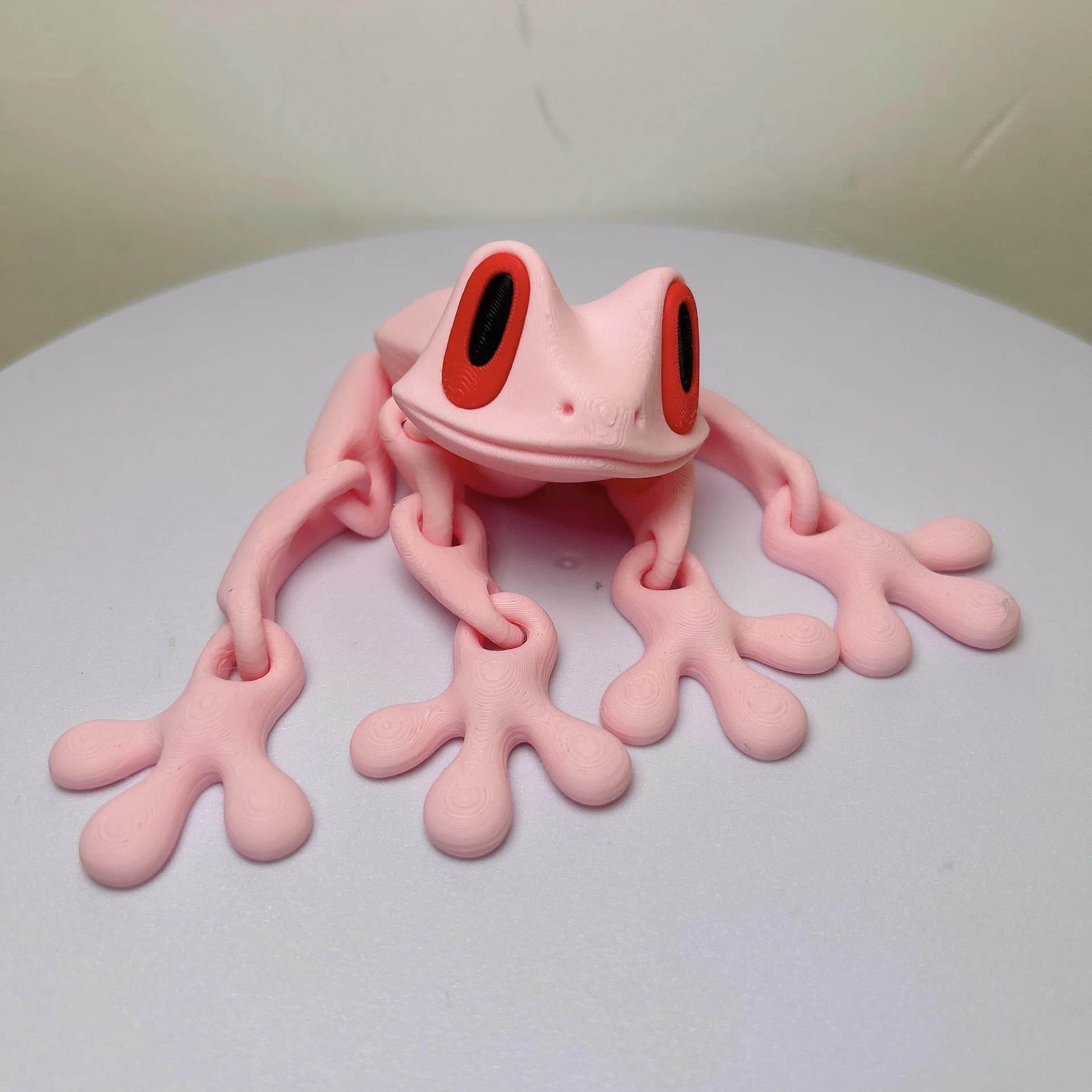Pink 3D printed magnetic frog toy with red oval eyes and four extended legs.