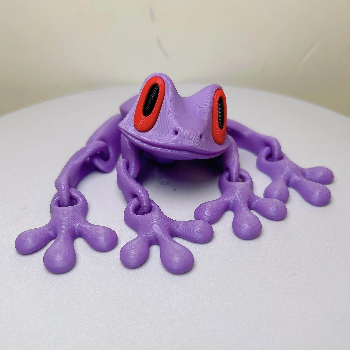 Lavender 3D printed magnetic frog toy with red oval eyes and four extended legs.