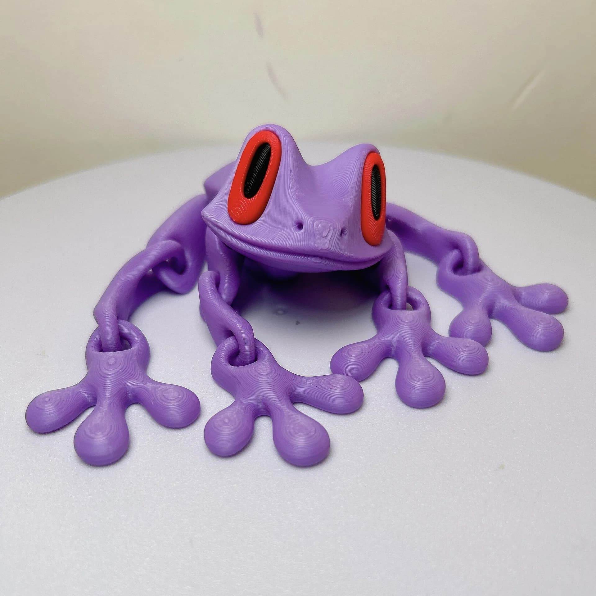 Lavender 3D printed magnetic frog toy with red oval eyes and four extended legs.