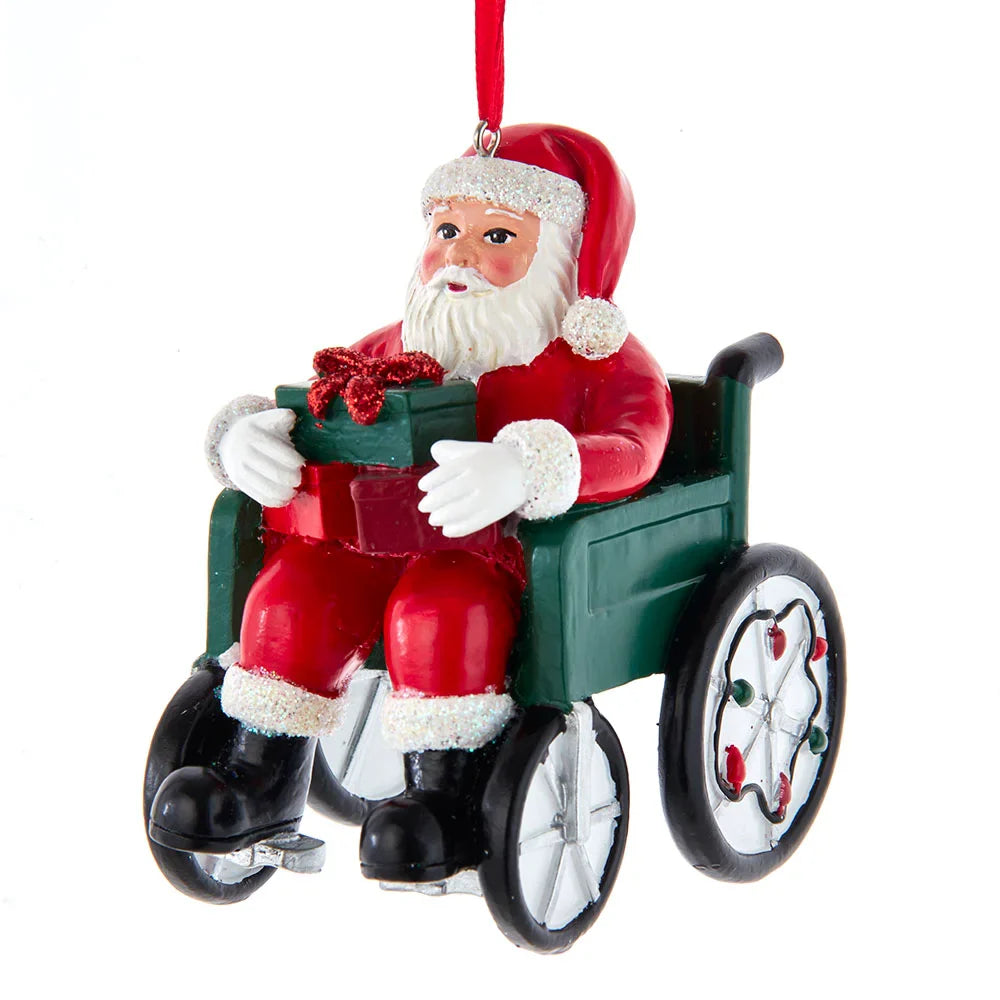 Santa in wheelchair ornament, red coat, white beard, holding green gift box