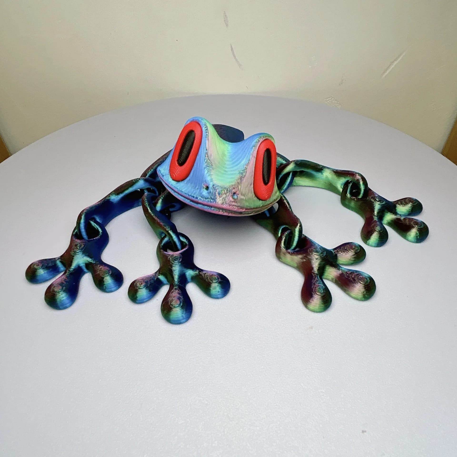 Iridescent blue-green 3D printed magnetic frog toy with red oval eyes and four legs.