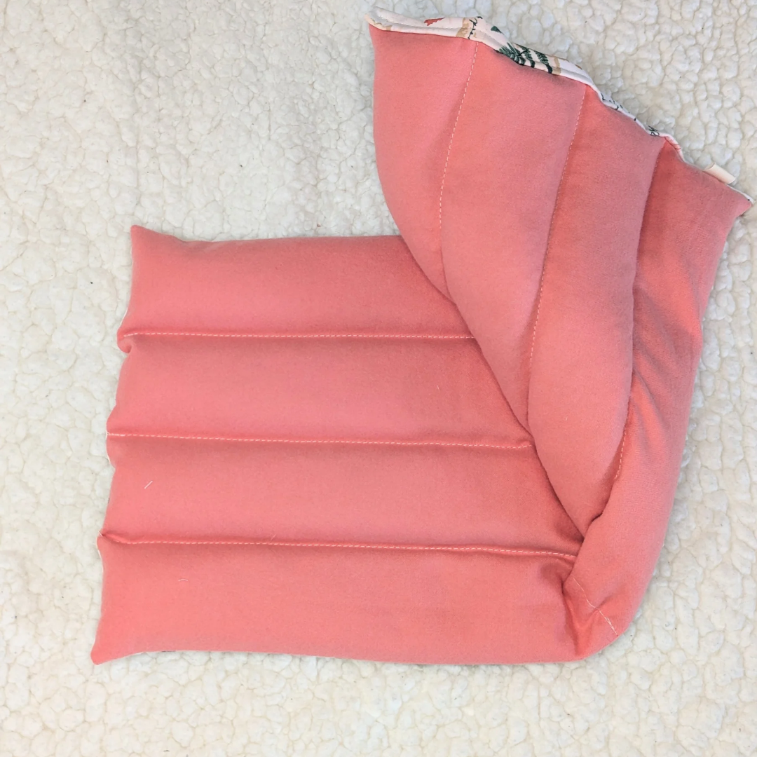 Folded weighted heating pad showing solid pink flannel layers and corner seam