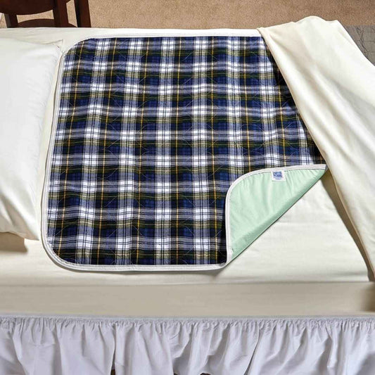 Plaid underpad with navy, green, and yellow checks and white trim; folded corner shows backing