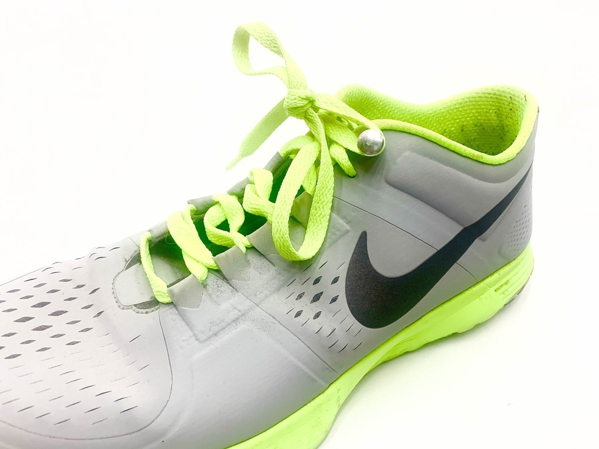 Athletic shoe with neon green laces and silver lace button, grey upper with dark swoosh