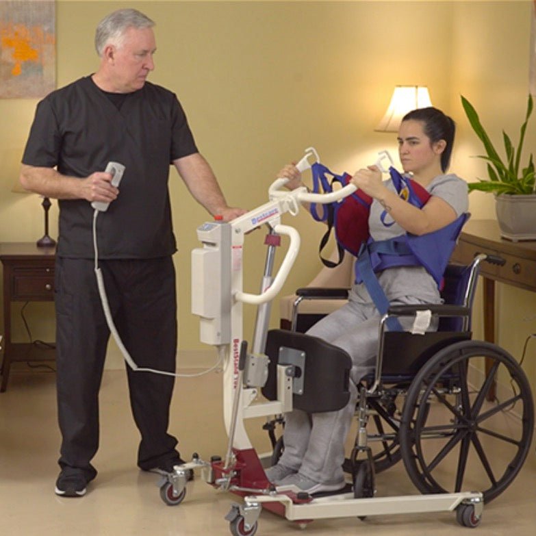 Sit-to-stand lift for home use with padded supports and hand handles, shown with wheelchair