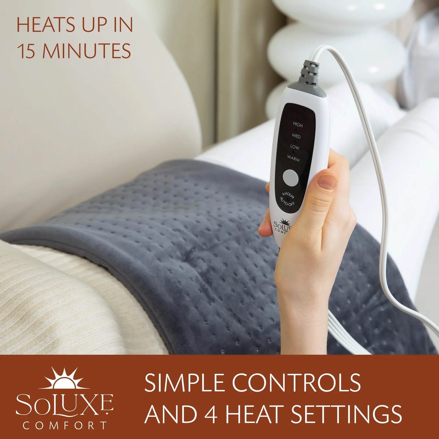 Dark gray heating pad on bed with controller in hand and power cord