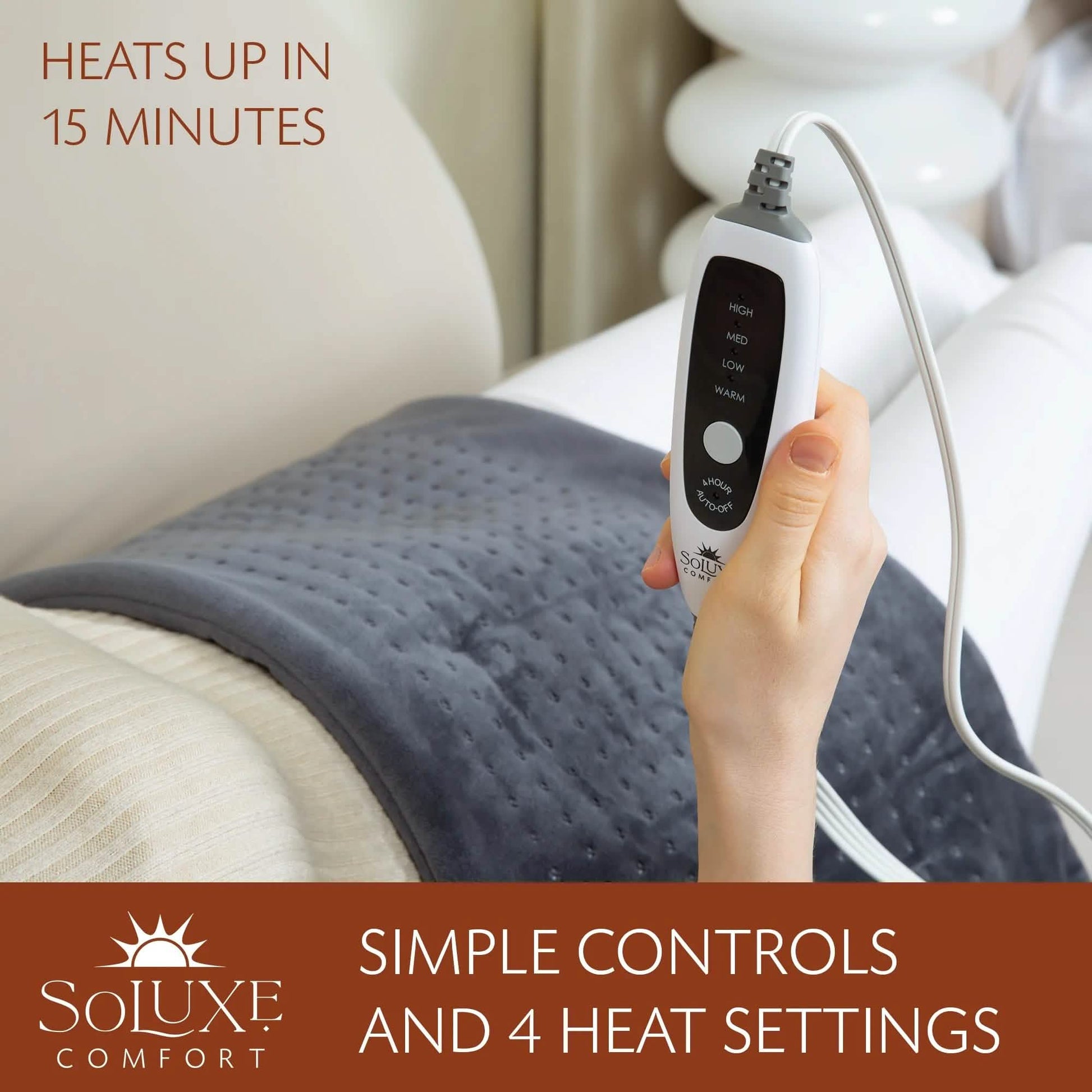 Dark gray heating pad on bed with controller in hand and power cord