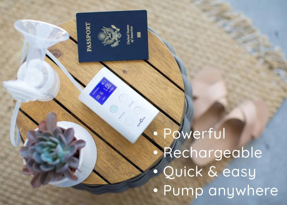 White portable rechargeable breast pump by Spectra with digital display, clear silicone flange, and travel accessories on wooden tray, top-down view