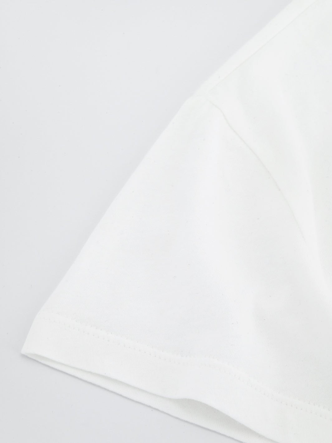 White boxy everyday tee sleeve close-up with visible stitching along hem.