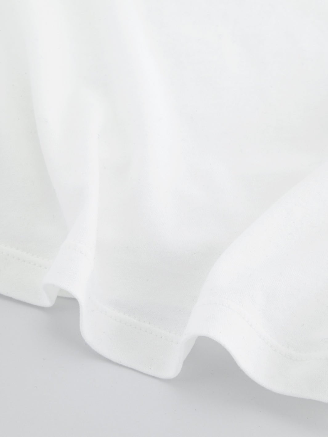 White boxy everyday tee fabric close-up at sleeve cuff and side seam.